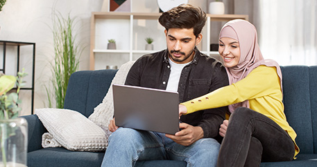  Ein Paar sitzt zusammen auf einem Sofa und betrachtet gemeinsam einen Laptop.