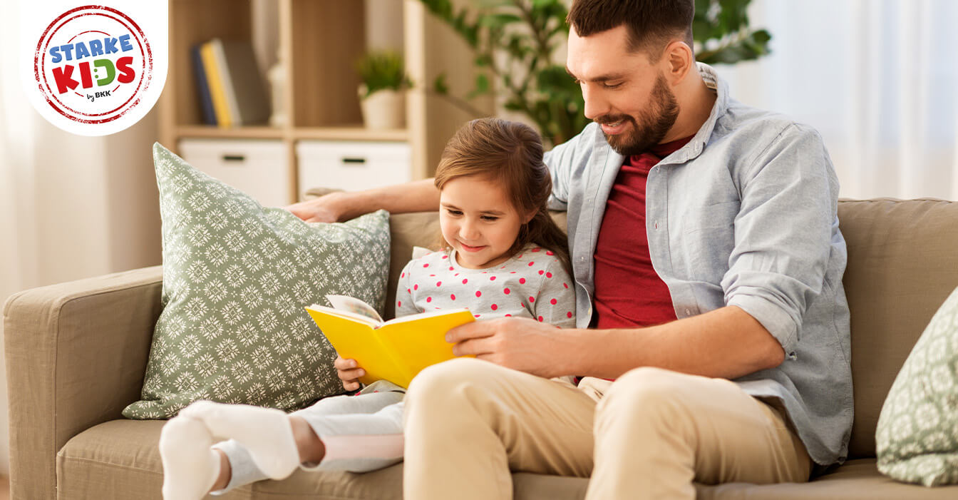 Ein Mann und ein Kind sitzen auf einem Sofa und schauen ein Buch.